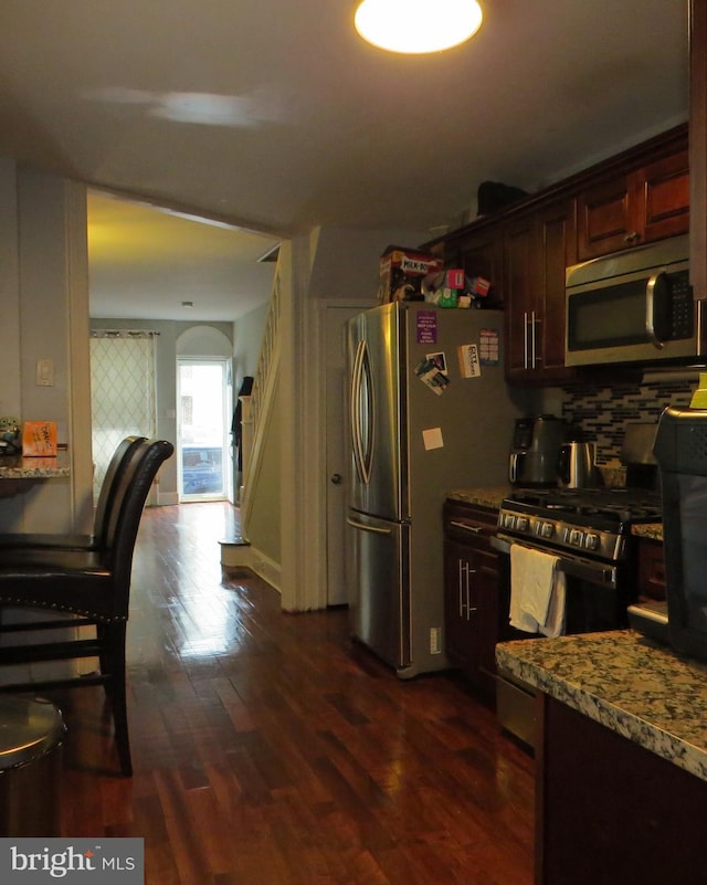 kitchen featuring appliances with stainless steel finishes, dark brown cabinetry, dark hardwood / wood-style floors, and light stone counters