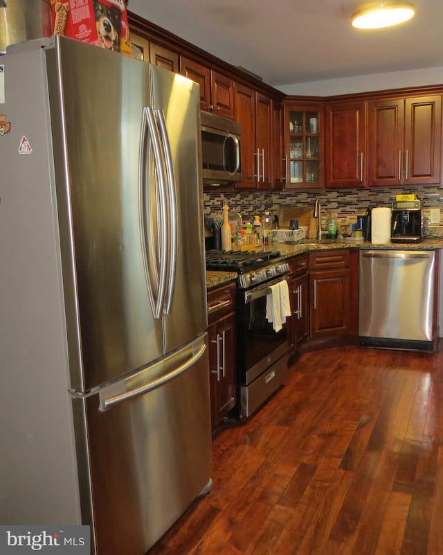 kitchen with dark stone countertops, stainless steel appliances, dark wood-type flooring, and decorative backsplash