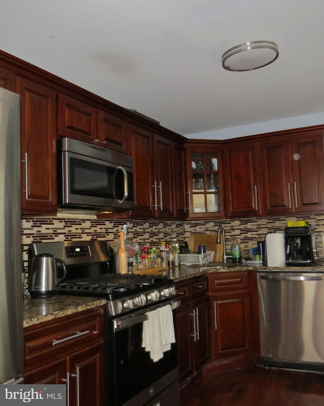 kitchen with appliances with stainless steel finishes, dark hardwood / wood-style flooring, dark stone counters, and tasteful backsplash