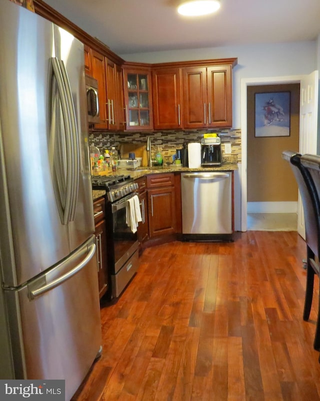 kitchen with appliances with stainless steel finishes, decorative backsplash, light stone countertops, and dark hardwood / wood-style flooring