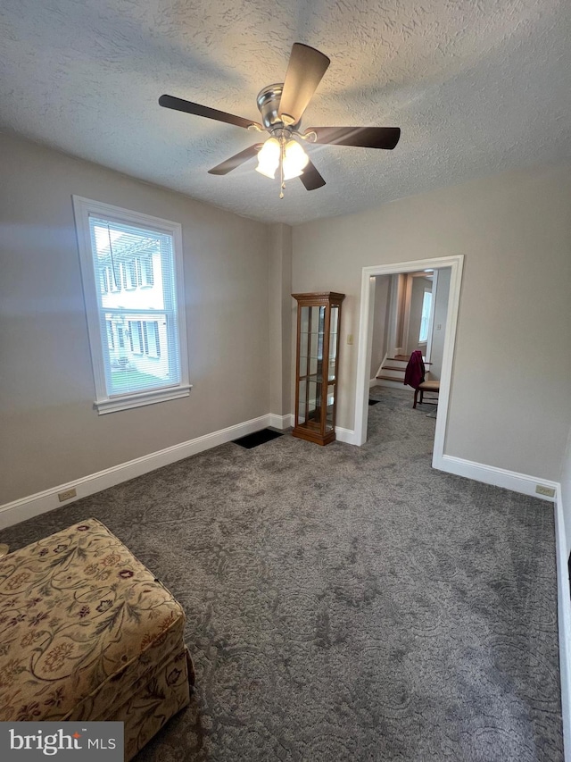 spare room featuring a textured ceiling, dark carpet, and ceiling fan