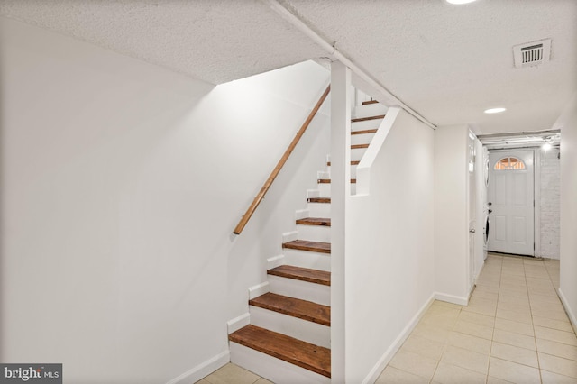 staircase with a textured ceiling and tile patterned floors