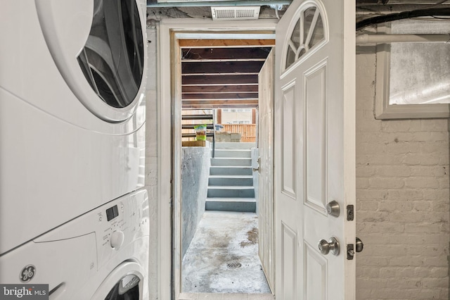 washroom with stacked washer and dryer and brick wall