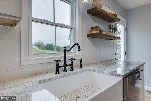 kitchen with light stone counters, backsplash, sink, and stainless steel dishwasher