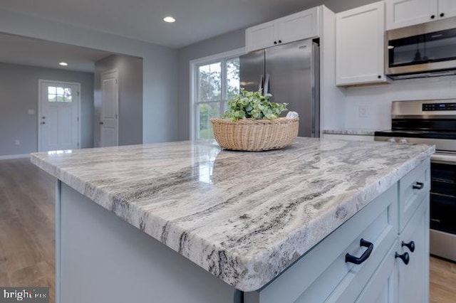 kitchen featuring light stone counters, white cabinets, a kitchen island, stainless steel appliances, and light wood-type flooring