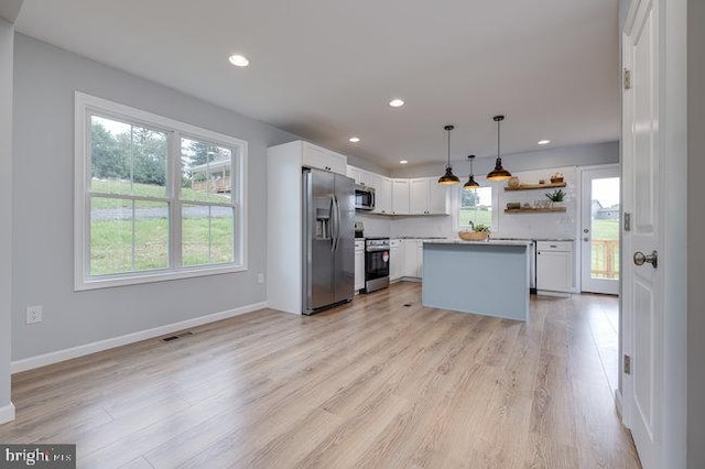 kitchen with pendant lighting, white cabinets, a kitchen island, appliances with stainless steel finishes, and light hardwood / wood-style floors