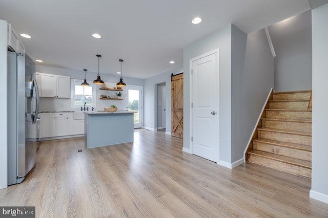 kitchen with white cabinets, a barn door, stainless steel refrigerator, a kitchen island, and pendant lighting