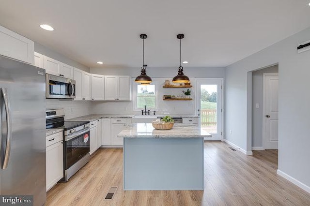 kitchen with light stone counters, white cabinetry, appliances with stainless steel finishes, a center island, and light wood-type flooring