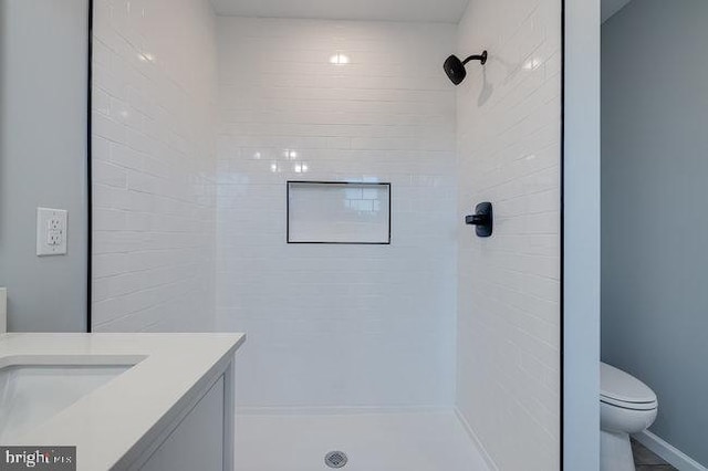 bathroom featuring a tile shower, vanity, and toilet