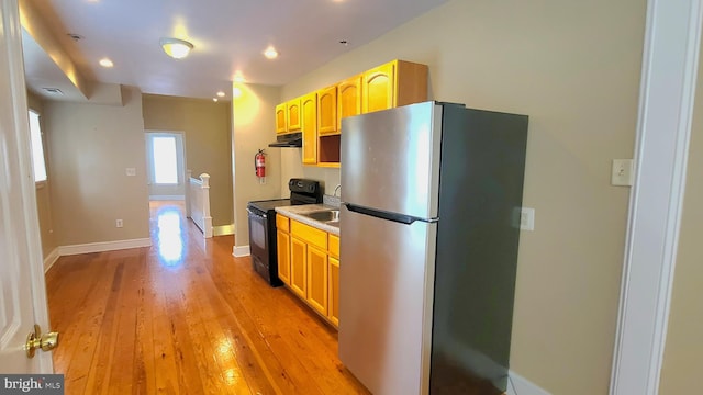 kitchen with black electric range oven, light hardwood / wood-style floors, light brown cabinetry, and stainless steel refrigerator