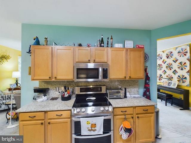 kitchen featuring appliances with stainless steel finishes, decorative backsplash, light wood-type flooring, and light stone countertops