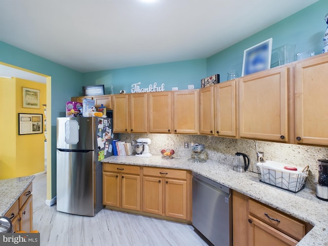 kitchen featuring appliances with stainless steel finishes, decorative backsplash, light wood-type flooring, and light stone countertops