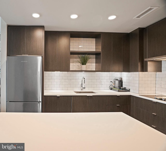 kitchen with black electric cooktop, backsplash, stainless steel fridge, and sink