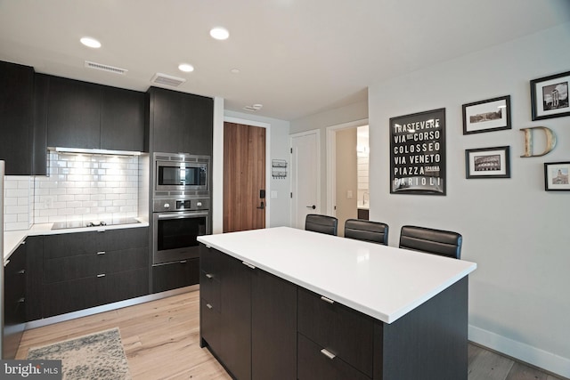 kitchen featuring appliances with stainless steel finishes, backsplash, light wood-type flooring, and a center island