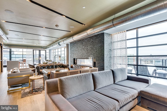 living room featuring light wood-type flooring, a multi sided fireplace, and a wall of windows