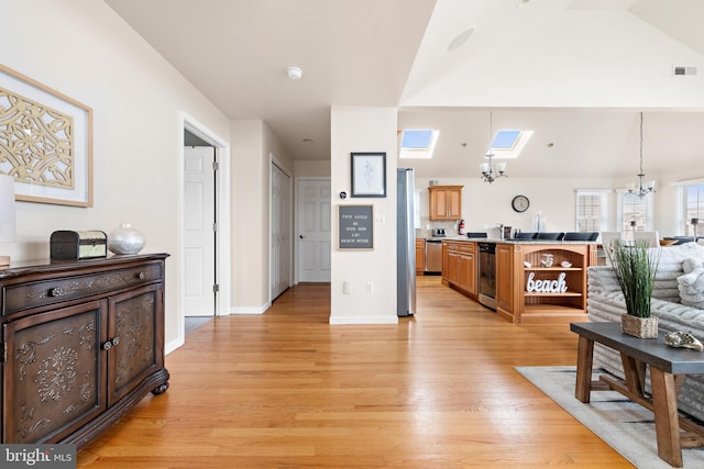 interior space with hanging light fixtures, light hardwood / wood-style floors, dishwasher, vaulted ceiling with skylight, and an inviting chandelier