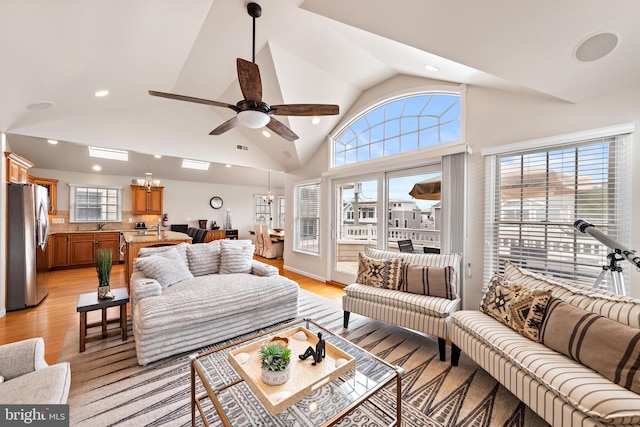 living room featuring ceiling fan with notable chandelier, light hardwood / wood-style floors, high vaulted ceiling, and sink