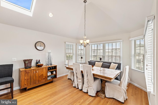 dining room with lofted ceiling with skylight, an inviting chandelier, and light hardwood / wood-style floors