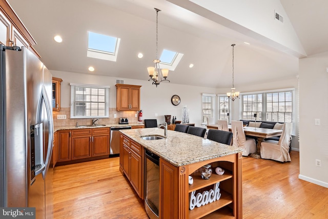 kitchen featuring an island with sink, stainless steel appliances, light wood-type flooring, and lofted ceiling with skylight