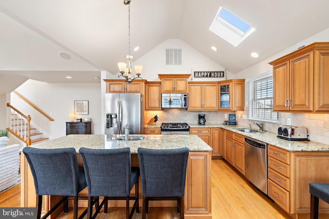 kitchen with light wood-type flooring, a kitchen island with sink, an inviting chandelier, stainless steel appliances, and a skylight