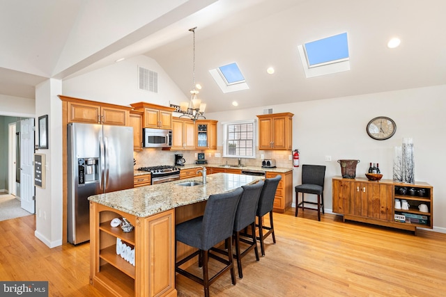 kitchen featuring a breakfast bar, stainless steel appliances, a skylight, a kitchen island with sink, and sink