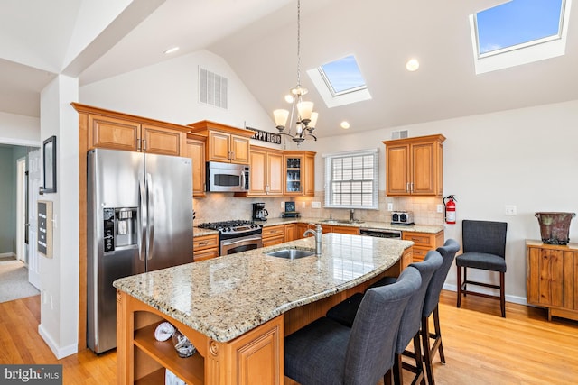 kitchen with light hardwood / wood-style floors, a kitchen island with sink, sink, a skylight, and appliances with stainless steel finishes