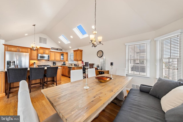 dining room featuring an inviting chandelier, vaulted ceiling with skylight, and light hardwood / wood-style flooring