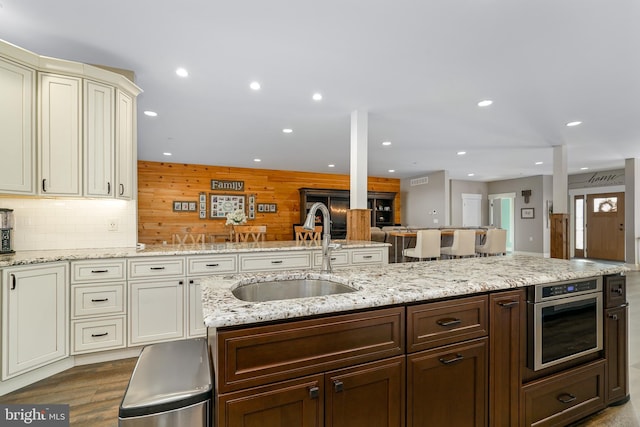 kitchen featuring light stone counters, stainless steel oven, wooden walls, sink, and light hardwood / wood-style flooring