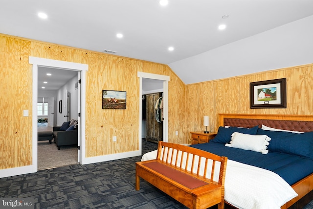 bedroom with dark carpet, vaulted ceiling, a spacious closet, a closet, and wood walls