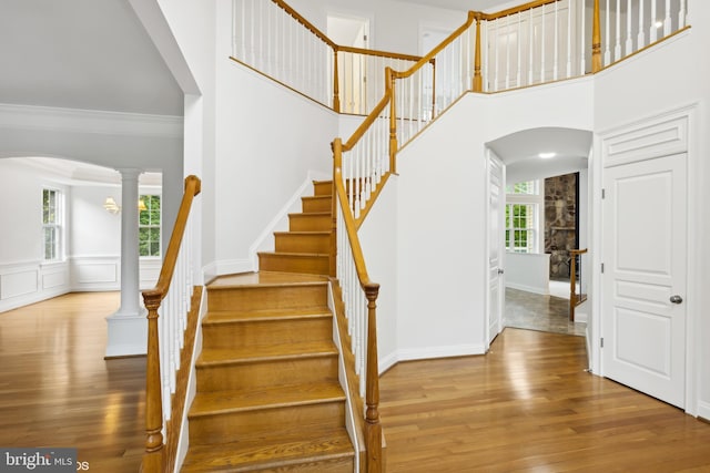 stairs with wood-type flooring, a towering ceiling, decorative columns, and crown molding