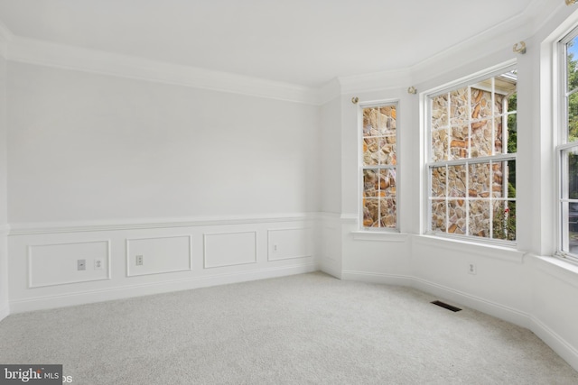 empty room with carpet flooring, a decorative wall, visible vents, crown molding, and wainscoting