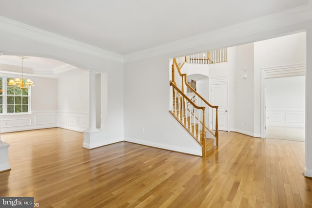 unfurnished room featuring a chandelier, light wood finished floors, ornate columns, stairs, and arched walkways