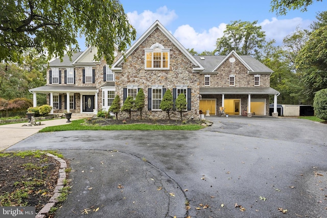 view of front of property featuring driveway, covered porch, stone siding, and a garage