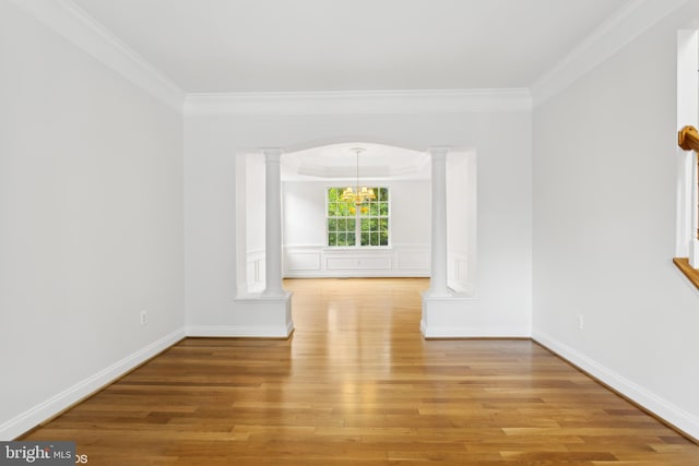 empty room featuring a notable chandelier, light wood-style floors, ornamental molding, and ornate columns