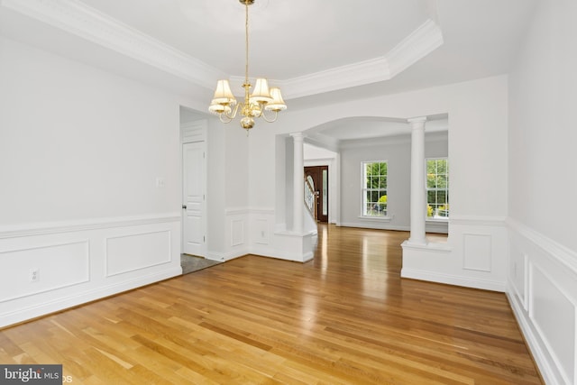 unfurnished dining area featuring ornamental molding, a chandelier, hardwood / wood-style flooring, and ornate columns