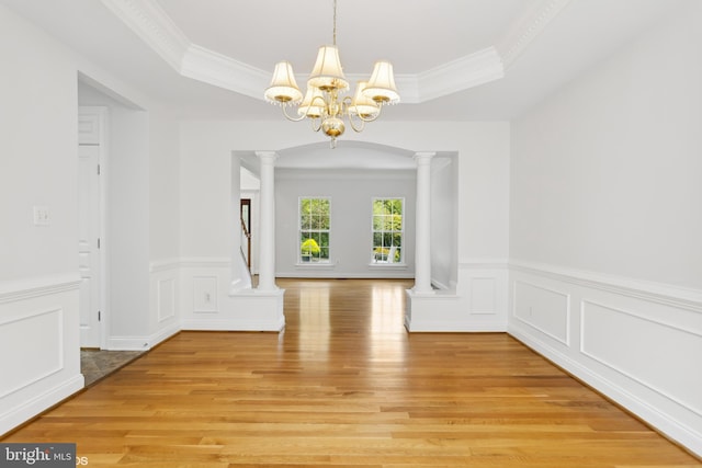 unfurnished dining area featuring a notable chandelier, crown molding, light hardwood / wood-style floors, and ornate columns