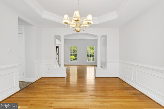 interior space featuring a tray ceiling, light wood-style flooring, a chandelier, and decorative columns