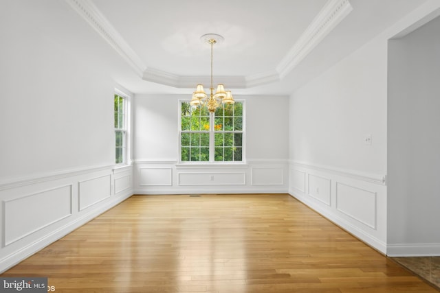unfurnished dining area with a chandelier, light wood finished floors, ornamental molding, a tray ceiling, and wainscoting