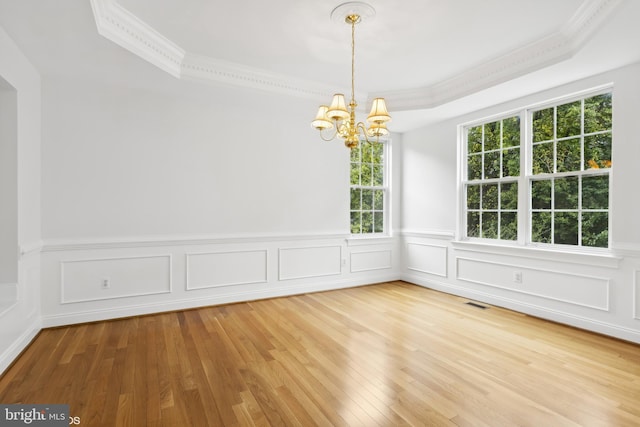 empty room with a tray ceiling, crown molding, a notable chandelier, and hardwood / wood-style flooring