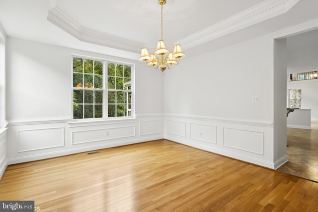 spare room featuring an inviting chandelier, crown molding, a tray ceiling, and hardwood / wood-style floors