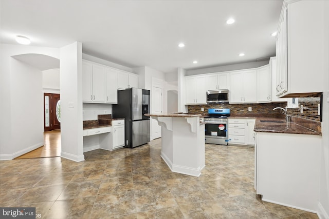 kitchen featuring appliances with stainless steel finishes, dark stone counters, white cabinetry, and a center island