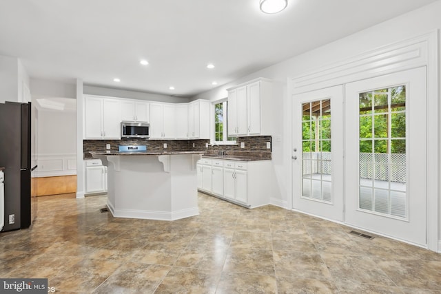 kitchen with backsplash, dark countertops, stainless steel appliances, and visible vents