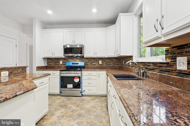 kitchen featuring a sink, appliances with stainless steel finishes, white cabinets, decorative backsplash, and dark stone counters