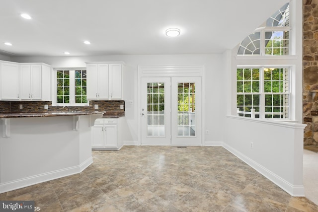 kitchen featuring dark stone countertops, white cabinets, a kitchen breakfast bar, and tasteful backsplash