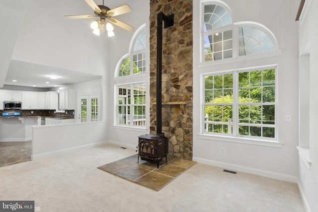 interior space featuring a high ceiling, ceiling fan, a wood stove, and a wealth of natural light