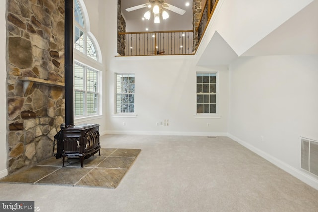 interior space with a wood stove, a towering ceiling, ceiling fan, and carpet flooring