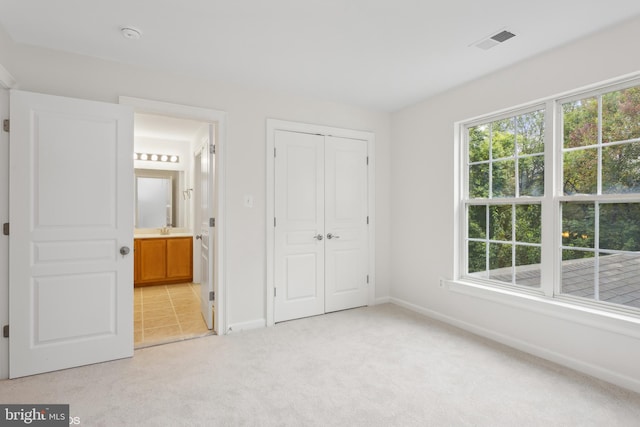 unfurnished bedroom featuring light colored carpet, baseboards, ensuite bath, visible vents, and a closet