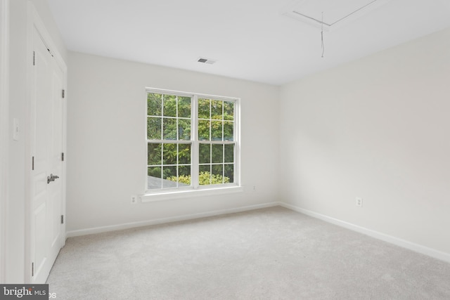 carpeted spare room featuring baseboards, visible vents, and attic access