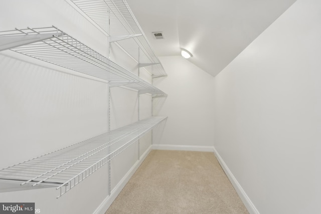 spacious closet with visible vents, vaulted ceiling, and light colored carpet