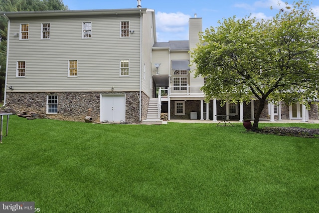rear view of property featuring stone siding, a patio, stairs, a chimney, and a lawn